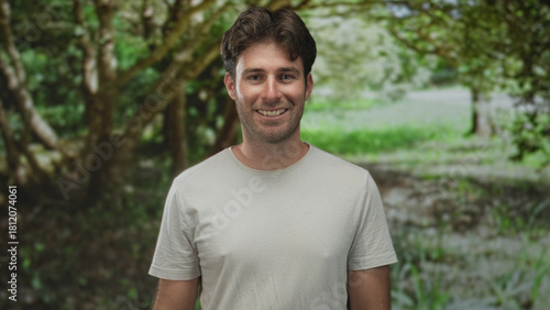 Man smiling with face visible and relaxed posture in a green park forest setting; serenity friendly.