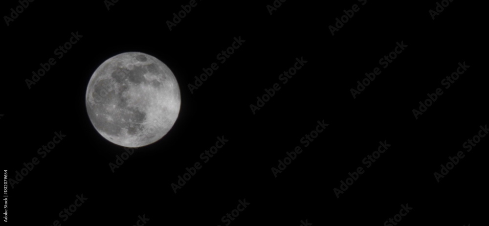 Fototapeta premium Photograph of an full moon in a dark sky. Image taken with a mobile phone lens with maximum zoom. Luminous moon with ethereal glow against pitch black sky. Supermoon, Night sky images 