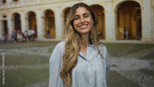 Fotografie Woman showing two finger peace sign and sticking tongue out in roman courtyard with archways and cobblestone plaza; playfulness joy spontaneity fun