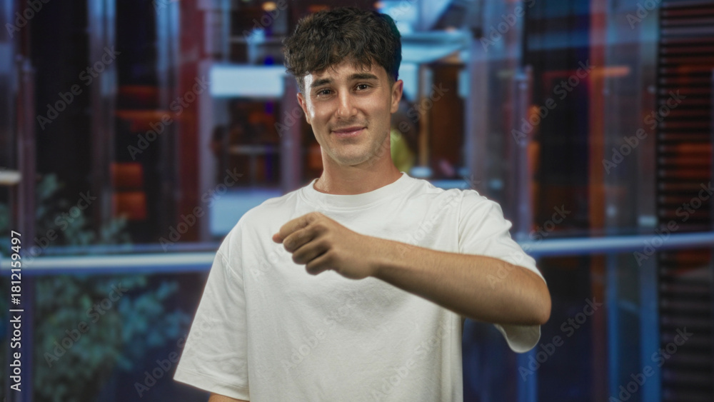Fototapeta premium Man pointing finger at camera in building lobby wearing white t shirt and relaxed expression; confidence invitation.