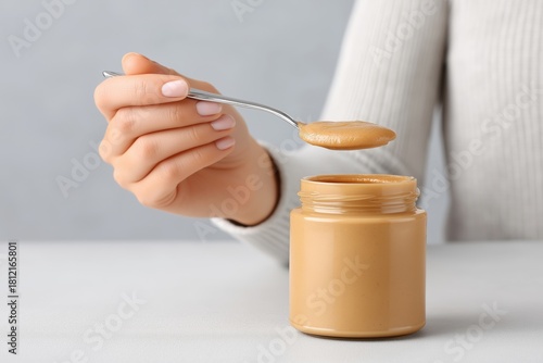 Female hand holding spoon with creamy peanut butter above jar, showcasing delicious texture and inviting presentation, perfect for culinary inspiration and food photography