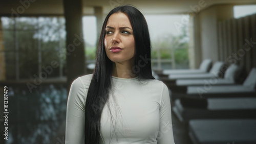 Young woman with long hair stands indoors at a spa pool, expressing a thoughtful and confident demeanor, surrounded by modern relaxation lounges in a serene atmosphere. Free Download Young woman with long hair stands indoors at a spa pool, expressing a thoughtful and confident demeanor, surrounded by modern relaxation lounges in a serene atmosphere. - GFXLoad