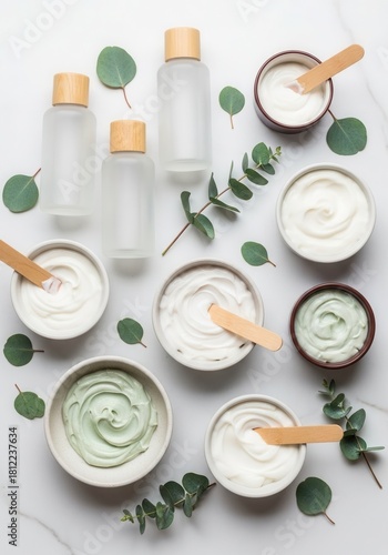 A variety of skincare products on a white surface with eucalyptus leaves