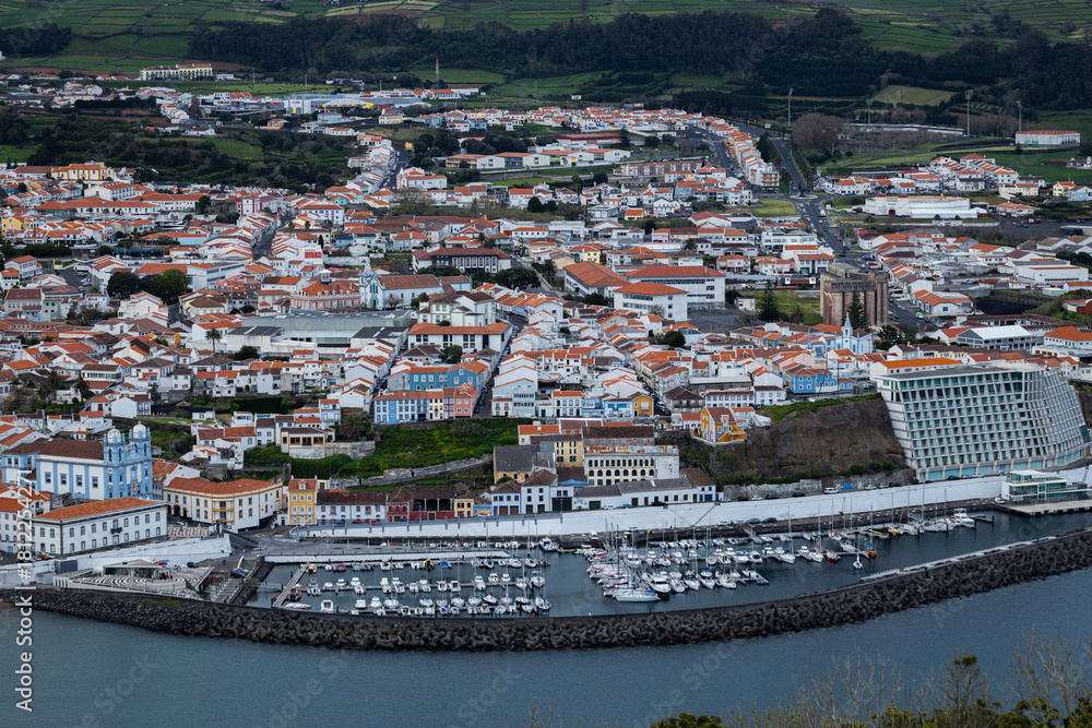 Obraz premium Aerial view of Angra do Heroísmo on Terceira Island, showcasing the town’s colorful rooftops, coastline, and lush volcanic landscape in the Azores, Portugal