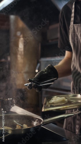 Vertical side view shot of young male chef carefully laying out seafood meat on frying pan while cooking in restaurant kitchen