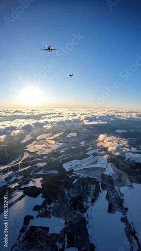 A large military plane and a parachutist jumping out of it against the background of the setting sun, clouds and a snow-covered landscape, aerial view from above.
