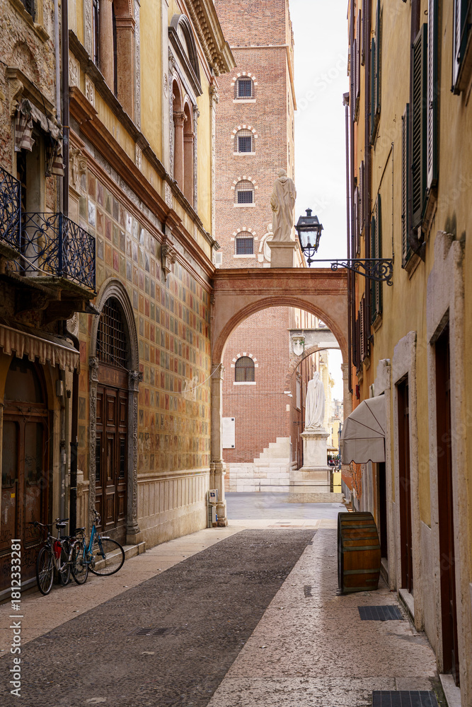 Fototapeta premium An old street with a statue on it in the city of Verona, Italy On the right building there is a lantern with an iron holder, on the left side there are a couple of bicycles parked