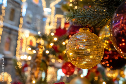 A close-up of a decorated Christmas tree on a background of decorated city buildings lit up with Christmas lights. Festive illuminations in the streets of the city background.