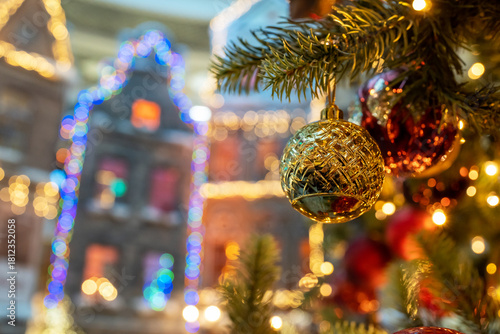A close-up of a decorated Christmas tree on a background of decorated city buildings lit up with Christmas lights. Festive illuminations in the streets of the city background.