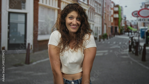 Woman smiling with exposed waist and relaxed posture on a city street, leaning slightly forward in a casual crop top; urban confidence joy.
