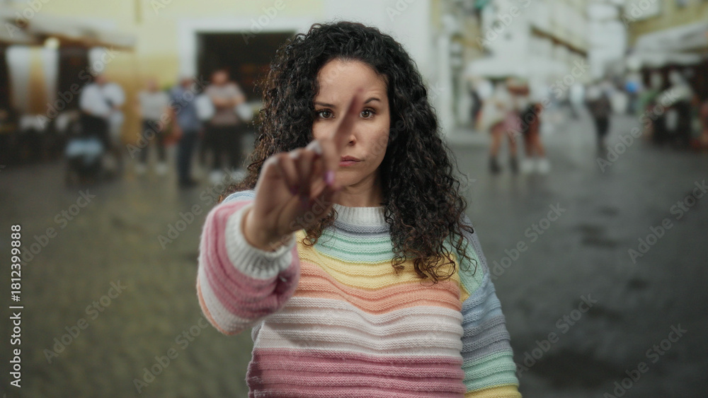Fototapeta premium Woman in colorful sweater outdoors on street showing rejection with crossed arms and serious expression amid blurred urban background depicting disagreement
