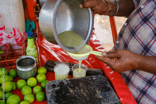 Indian street vendor pouring fresh sugarcane juice into glass at roadside stall with limes, highlighting traditional summer drink preparation and vibrant local market scene
