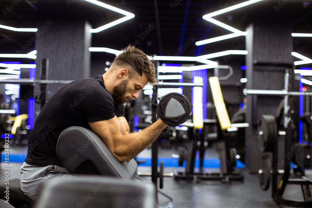 Naklejka premium Man exercising with dumbbell in modern gym during daytime