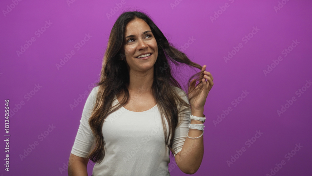 Obraz premium Young hispanic woman smiling, touching hair and wrist bracelets in purple studio setting; playfulness.