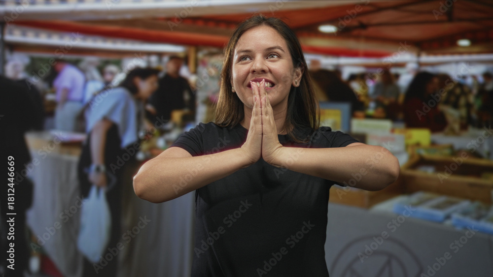 Fototapeta premium Woman pressing palms together at a bustling outdoor market stall in the city, looking upward; gratitude souvenir memory.