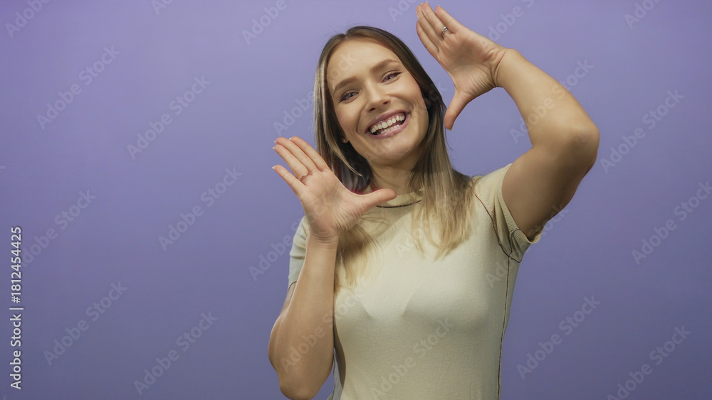 Fototapeta premium Woman smiling against a purple background, hands framing face, expressing joy and positivity.