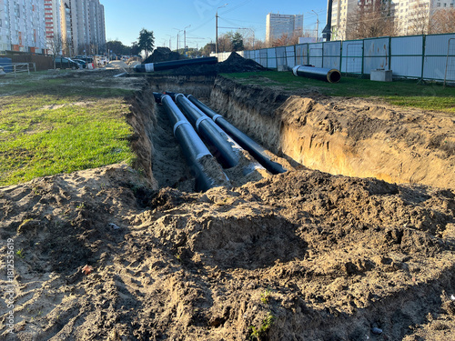 Large trench with newly installed insulated steel pipes for district heating or water supply in city residential area, concept of urban infrastructure, utility repair and civil engineering works.