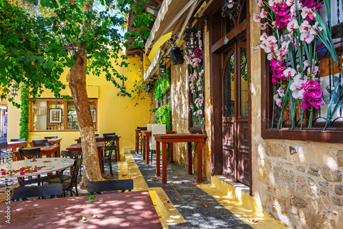 Fototapeta Naklejka Na Ścianę i Meble -  An outdoor patio with tables and chairs at a colorful cafe in the medieval old town of Rhodes, Greece, on the island of Rhodes.