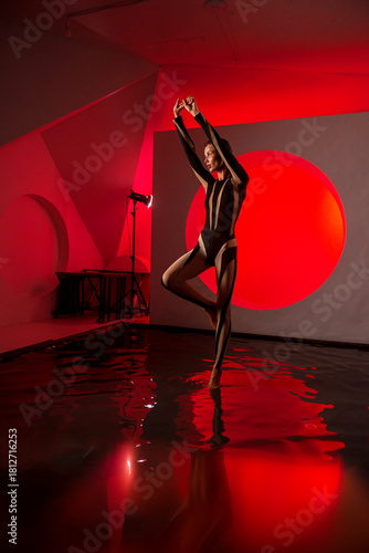 A slender, athletic woman poses in a studio against a red backdrop.