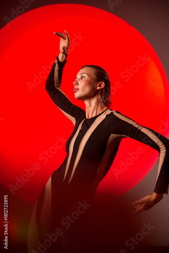 A slender, athletic woman poses in a studio against a red backdrop.