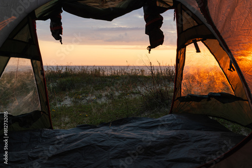 Fototapeta Naklejka Na Ścianę i Meble -  Scenic view from inside a camping tent looking at a golden sunset over the Baltic Sea coast in Estonia.