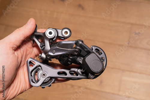 Close-up of a hand holding a modern rear derailleur showing jockey wheels and mounting interface