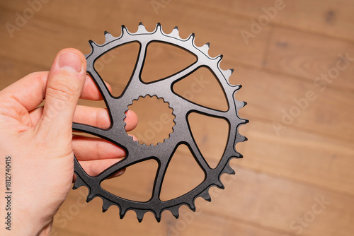 Close-up of a hand holding a black bicycle chainring with spline interface and weight-reducing cutouts