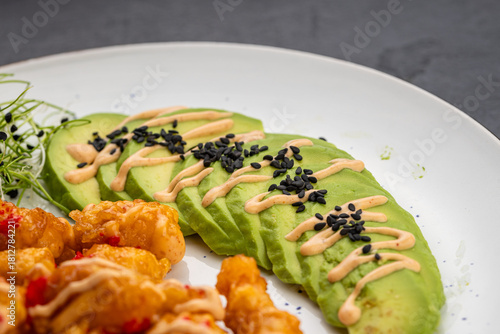 Sliced avocado with spicy mayo and black sesame on white plate, close up