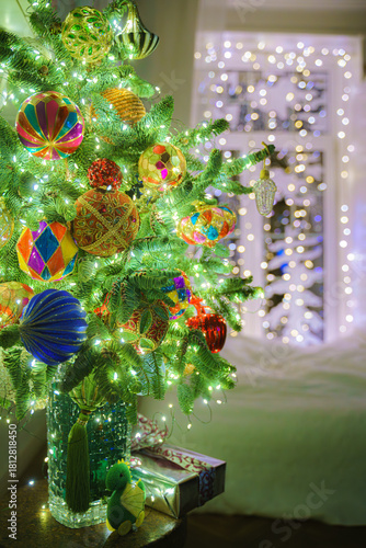 Vertical view of Christmas tree standing in vase decorated with Christmas balls and garland, toys and gifts are lying under it, in background is blurred window with garland, Saint-Petersburg, Russia