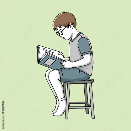 Young boy with glasses sitting on a stool reading a book intently.