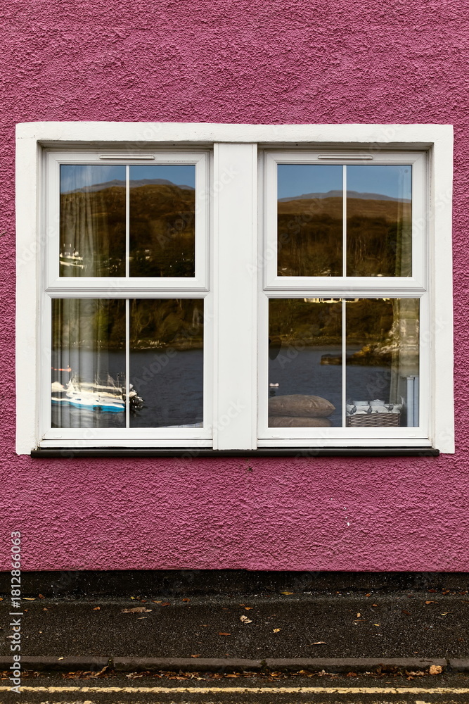 Fototapeta premium Glazed, double hung window reflecting the harbor with some boats, set in a purplish-pink painted, ancient fisherman's house. Portree-Skye-Scotland-091