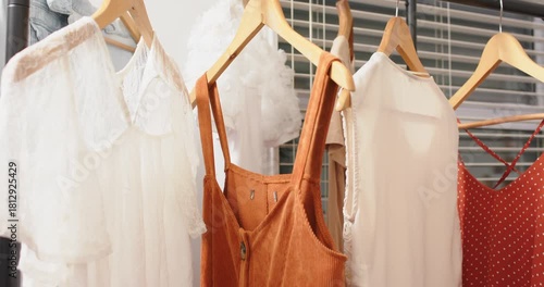 wooden hangers on metal rack swaying clothes against shop blinds, camera panning showing colors