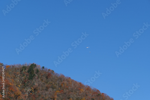 紅葉の山と物資を運ぶヘリコプター