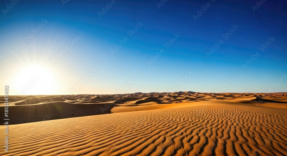 Naklejka premium Expansive desert landscape with rolling sand dunes under a brilliant clear blue sky and the bright sun casting strong sunlight during a warm, sunny day.