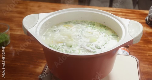 Woman cooking broccoli soup and adding chopped green onions, Female hands adding spring onions to boiling broccoli soup, Broccoli cream soup with vegetables boiling in pot.
