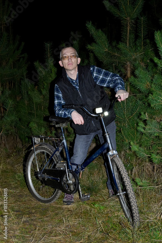 portrait of man with bicycle in night forest looking directly at camera lens