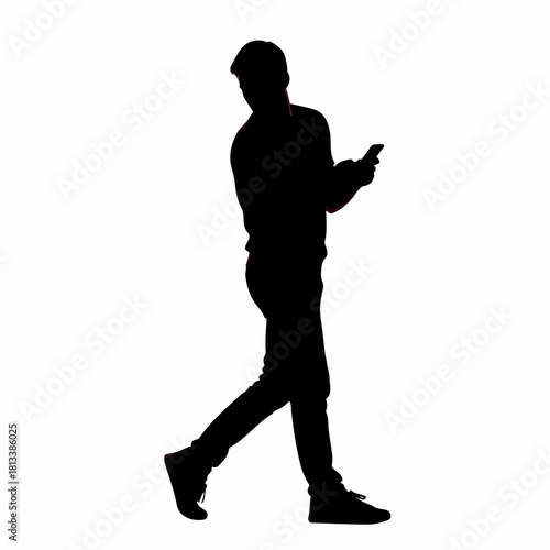 Silhouette of a young man walking while looking at his smartphone.
