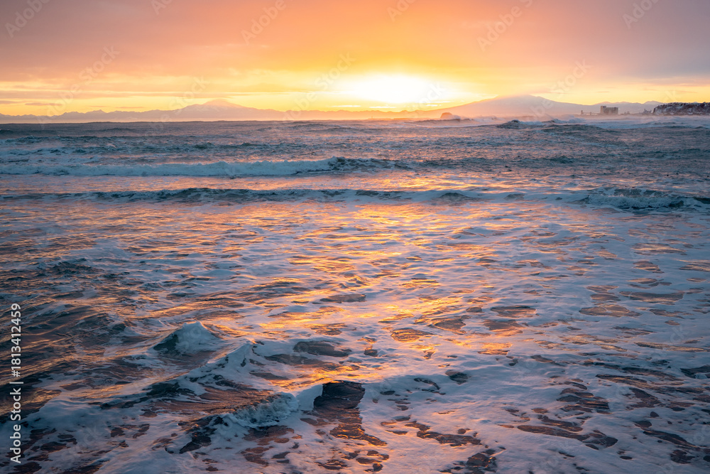 Obraz premium Sunrise colors reflecting on waves of the Sea of Okhotsk in Abashiri, Hokkaido, with distant Shari and Umabetsu mountains creating a stunning winter coastal landscape