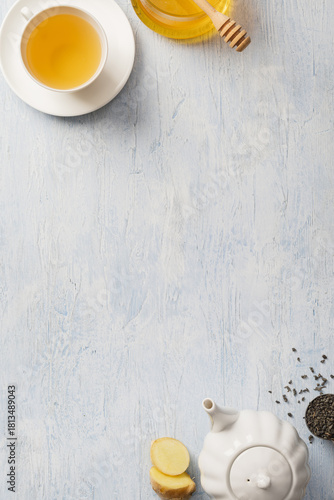 Flat lay of a warm herbal tea setup with ginger, lemon, honey, and loose tea leaves on a textured light surface, ideal for wellness, health, and lifestyle themes. Light background.