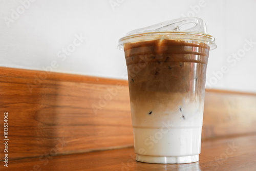 Iced coffee in a plastic cup  Separate layers of coffee and milk placed on a white table.