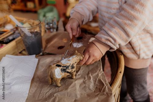 Photography Child painting a small toy cow with white and black acrylics.