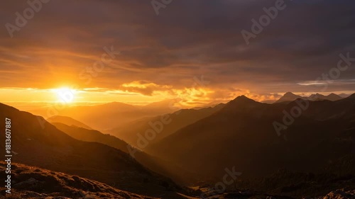 A breathtaking nature landscape at sunset and sunrise features orange clouds over mountain peaks and desert hills during a misty morning dawn