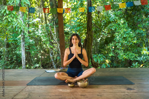 Woman meditating cross-legged with singing bowls in forest studio.