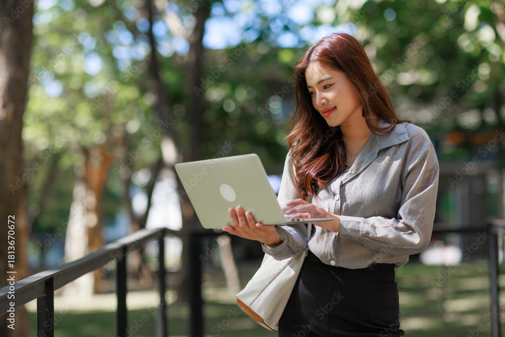 Obraz premium Young asian woman working online standing with laptop outdoors