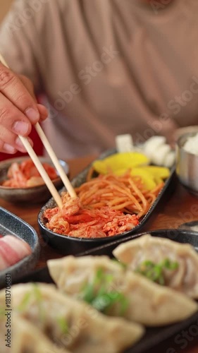 A man eats kimchi, banchan, and other Korean appetizers with chopsticks in a restaurant. Fermented food, traditional Asian meals.