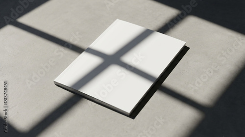 Clean Blank White Book Mockup, Lying on a Light Grey Concrete Floor with Striking Window Shadows and Sunlight.