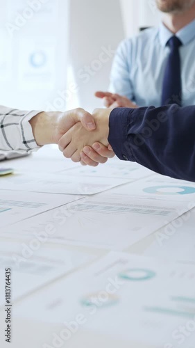 Business people partners shaking hands in office with financial charts, laptop and reports on table, symbolizing success, teamwork, agreement, collaboration and corporate growth