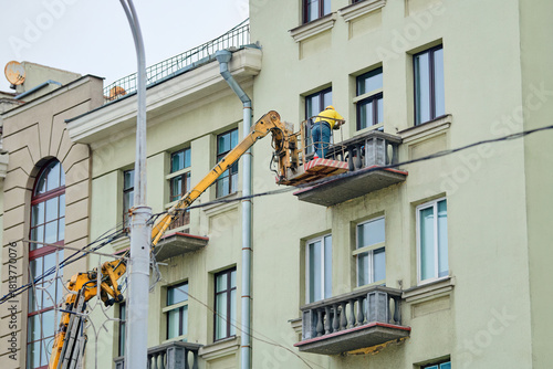 Construction worker on aerial platform repairing and renovating balcony for structure improvement, building exterior renovation. Building under repair, worker reinforcing balcony using lift platform