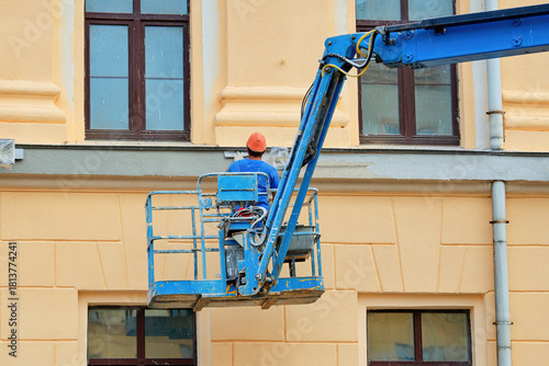 Worker plastering building, plastering job underway on historic building facade with worker on elevated platform applying cement to wall surface as part of exterior renovation work