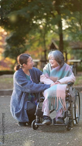 秋の紅葉で介護する女性と車椅子の高齢者の見つめ合う介護士のような人　縦動画　紅葉の前ボケあり